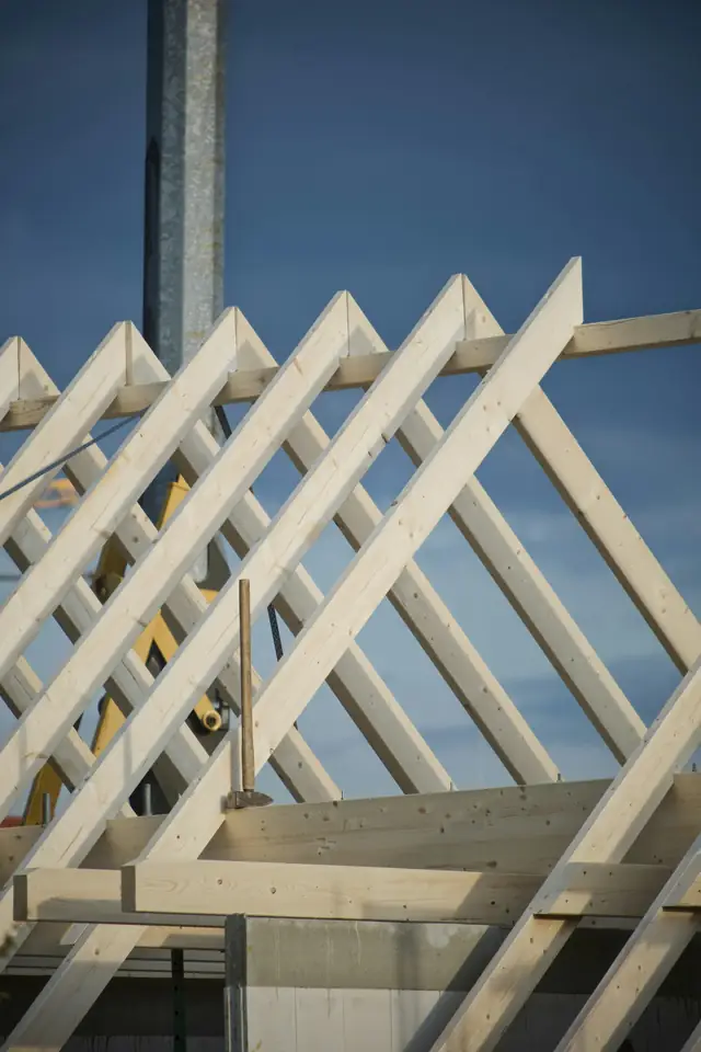 Chevrons de bois clair d'une charpente neuve se découpant sur le ciel bleu