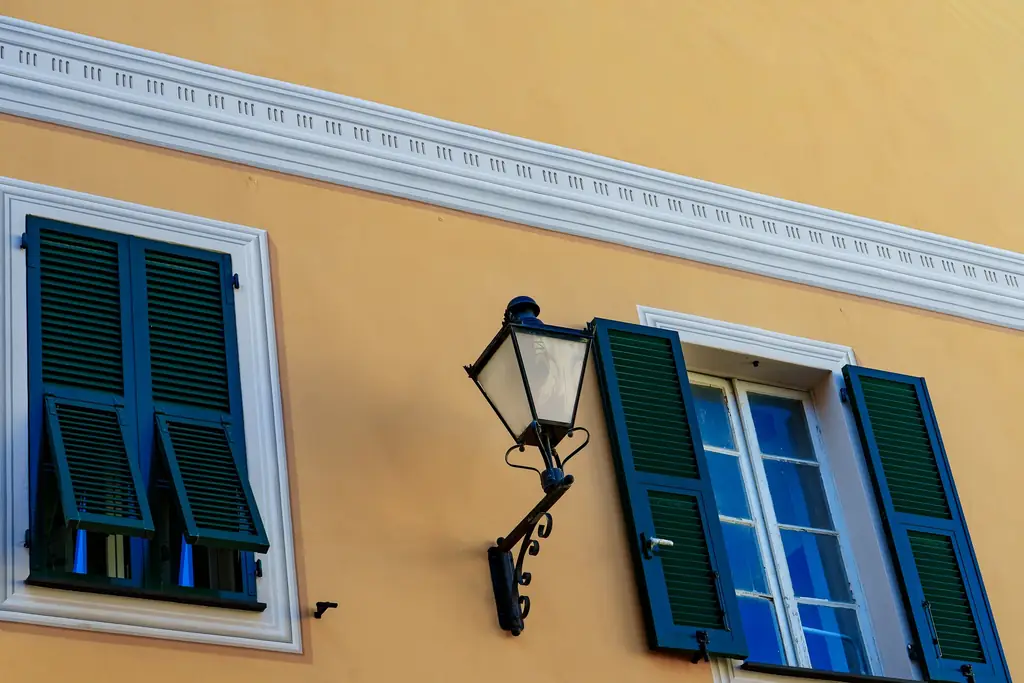 Façade jaune ocre aux volets verts, lanterne en fer forgé et encadrements blancs
