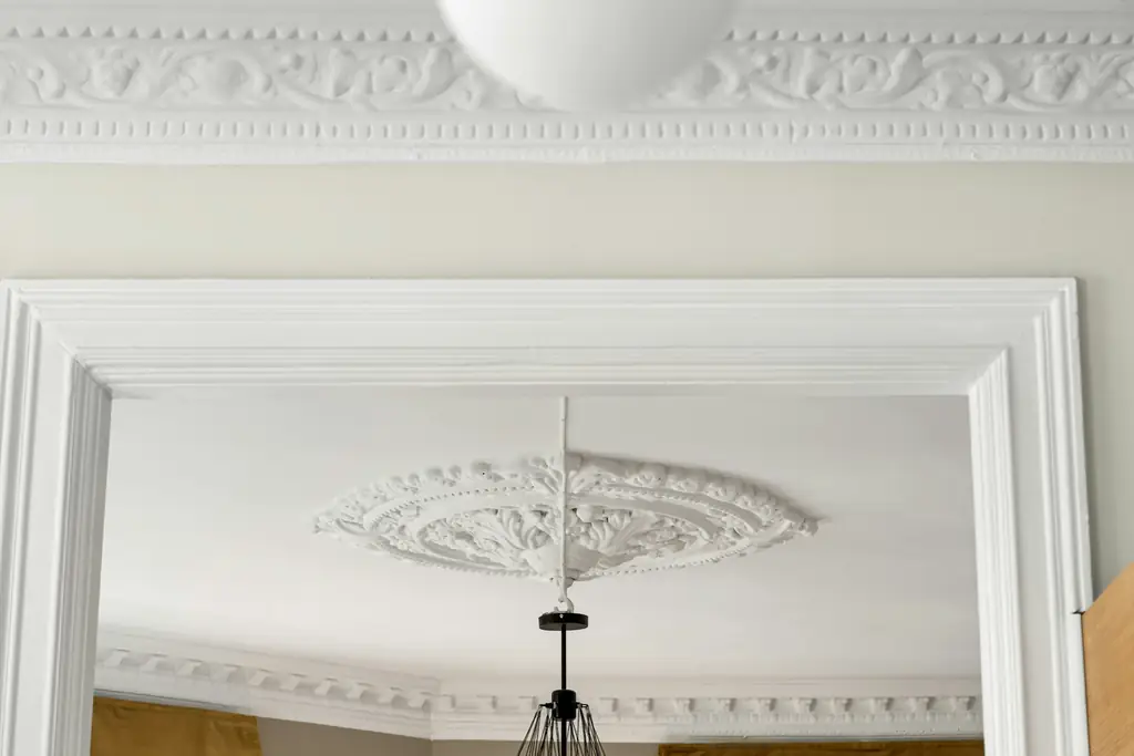Plafond ancien avec rosace et corniches moulurées, vu à travers l'encadrement d'une porte