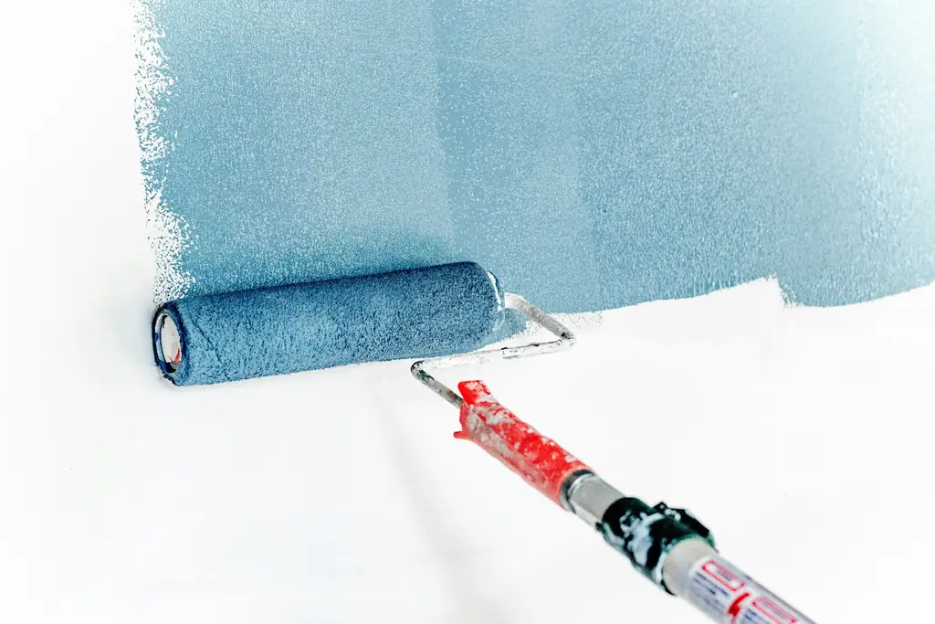 Rouleau chargé de peinture bleue passé sur un mur blanc