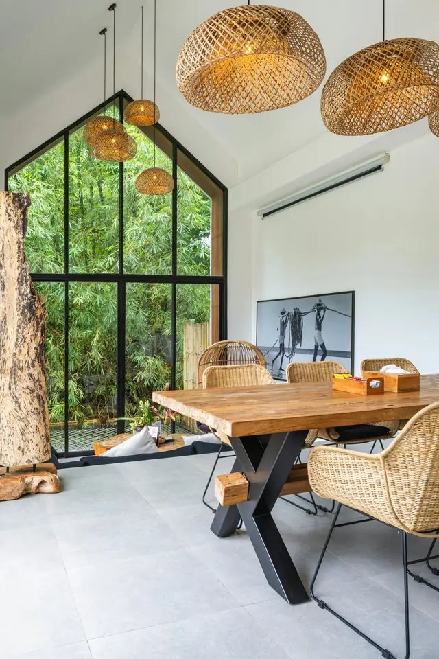 Sol gris lisse d'une salle à manger, table en bois, suspensions en rotin, grande baie vitrée