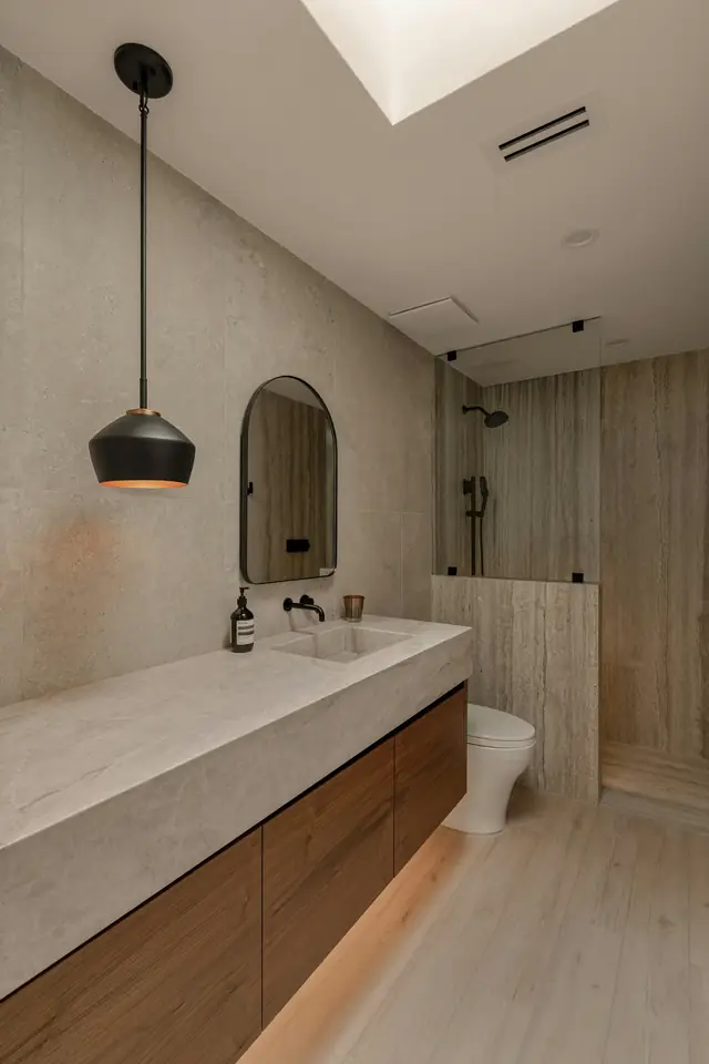 Salle de bain minérale : plan vasque gris clair sur meuble en bois, miroir en arche, suspension noire